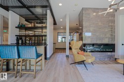Spacious lounge area featuring a large format tile fireplace with an integrated linear firebox, wood-finish flooring, a built-in bar with dark countertops and shelving, and a decorative ceiling grid - 