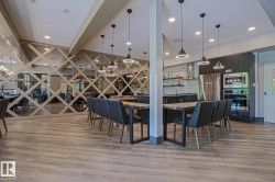 Spacious communal area featuring light wood-finish flooring, a contemporary kitchen with stainless steel appliances, dark cabinetry, and integrated lighting - 