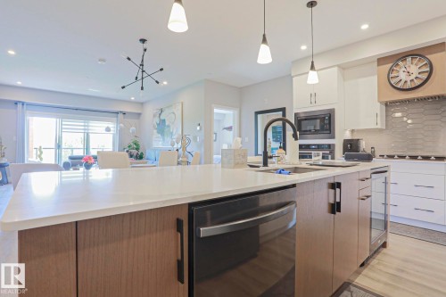 Kitchen island with a white countertop and integrated dishwasher, featuring a matte black faucet and pendant lighting - 211 7463 May Common, Edmonton, AB 