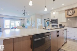 Kitchen island with a white countertop and integrated dishwasher, featuring a matte black faucet and pendant lighting - 