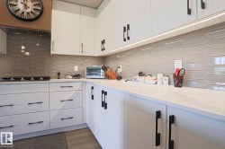 Contemporary kitchen featuring white cabinetry with matte black hardware, light-toned countertops, and a patterned tile backsplash - 