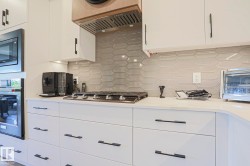 Contemporary kitchen featuring white cabinetry with black hardware, a gas cooktop, quartz countertops, a neutral geometric tile backsplash, and a built-in oven and microwave - 