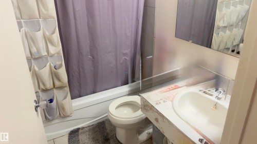 Bathroom featuring a white porcelain toilet, a built-in vanity with an integrated sink, a wall-mounted mirror, and a full-size bathtub - 311 8604 Gateway Boulevard, Edmonton, AB 