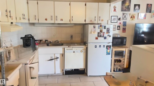Kitchen featuring white cabinetry, tile backsplash, laminate countertops, a stainless steel sink, and white appliances - 311 8604 Gateway Boulevard, Edmonton, AB 
