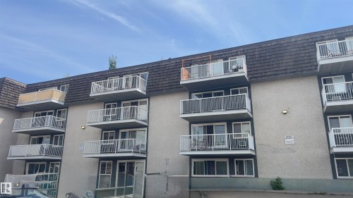 Multi-story apartment building with stucco exterior, individual balconies with white railings, dark grey shingled mansard roof, and multiple large windows - 311 8604 Gateway Boulevard, Edmonton, AB 