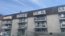 Multi-story apartment building with stucco exterior, individual balconies with white railings, dark grey shingled mansard roof, and multiple large windows - 311 8604 Gateway Boulevard, Edmonton, AB 