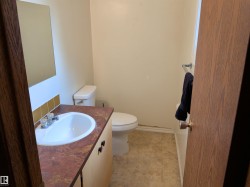 Bathroom featuring a light wood-finish vanity with a built-in sink, a mottled brown countertop, a wall mirror, and a white toilet - 