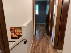 Hallway featuring wood-finish flooring, white walls, and dark wood-stained interior doors - 
