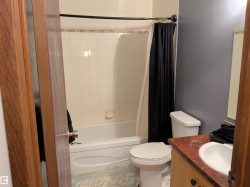 Bathroom featuring a white bathtub with subway tile surround, a porcelain toilet, and a vanity with a recessed sink and wood-finish countertop - 
