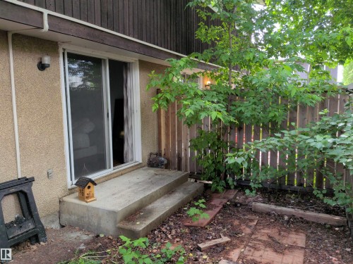 Concrete patio with a sliding glass door entry, bordered by a wooden privacy fence and mature trees - 2724 105 Street Nw, Edmonton, AB - Outdoor