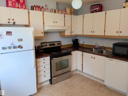 Kitchen featuring white cabinetry with wood trim and round knobs, a stainless steel range, a double basin stainless steel sink, and a white refrigerator - 