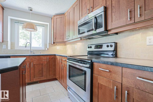 Kitchen featuring wood cabinetry, stainless steel appliances, dark countertops, a light tile backsplash, and a window above the sink - 17811 62C Avenue, Edmonton, AB 