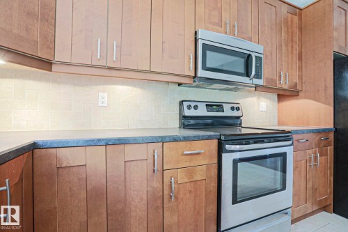 Kitchen featuring wood cabinetry, stainless steel appliances, dark countertops, and a subway tile backsplash - 17811 62C Avenue, Edmonton, AB 