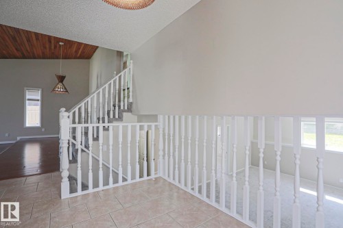 Foyer featuring light-toned tile flooring, white baluster railings, and a vaulted ceiling with wood-finish paneling - 17811 62C Avenue, Edmonton, AB 