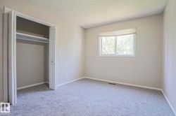Carpeted room featuring a white-framed window with a roller shade, light-toned walls, a closet with bi-fold doors, and ceiling texture - 