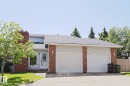 Exterior featuring a brick chimney, red brick accents, light-colored siding, a two-car garage, and a peaked roofline - 17811 62C Avenue, Edmonton, AB 