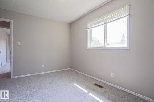 Spacious room featuring neutral carpeting, light-colored walls, and a large window with horizontal blinds - 17811 62C Avenue, Edmonton, AB 
