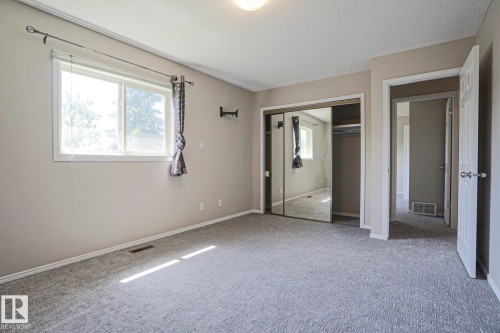 Carpeted interior space featuring a large window, neutral wall paint, white trim, and a mirrored closet - 17811 62C Avenue, Edmonton, AB 