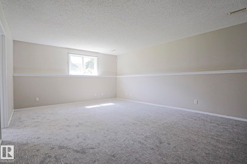 Spacious room featuring new carpeting, a textured ceiling, a single window, and a neutral two-tone wall paint scheme with a decorative chair rail - 17811 62C Avenue, Edmonton, AB 