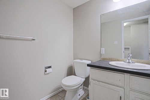 Bathroom featuring a white toilet, light-toned wall paint, and a vanity with a dark countertop and integrated sink - 17811 62C Avenue, Edmonton, AB 