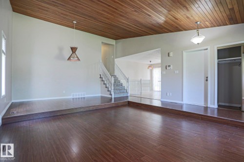 Open-concept living space featuring wood-finish flooring, a wood-paneled ceiling, and a prominent staircase with white railings - 17811 62C Avenue, Edmonton, AB 
