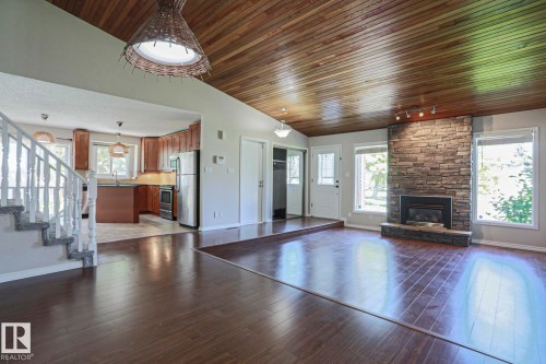 Spacious living area featuring wood-finish flooring, a vaulted wood-paneled ceiling, and a stone-clad fireplace with a gas insert - 17811 62C Avenue, Edmonton, AB 