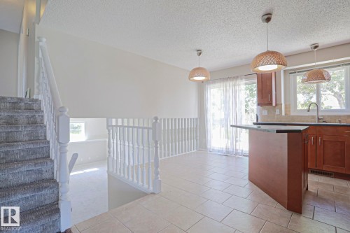 Open-concept living space featuring a carpeted staircase, white banister, and a kitchen area with wood cabinetry - 17811 62C Avenue, Edmonton, AB 