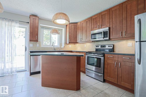 Kitchen featuring wood-finish cabinetry, stainless steel appliances, and a central island with countertop space - 17811 62C Avenue, Edmonton, AB 