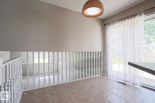 Tiled flooring, white baluster railing, a woven pendant light fixture, and a sliding glass door with sheer white curtains - 17811 62C Avenue, Edmonton, AB 