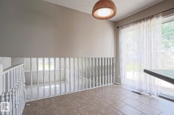 Tiled flooring, white baluster railing, a woven pendant light fixture, and a sliding glass door with sheer white curtains - 