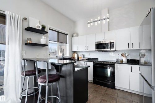Recently renovated kitchen  featuring open shelves, black electric range oven, backsplash, a kitchen breakfast bar, and freestanding refrigerator - 302 10905 109 Street, Edmonton, AB 