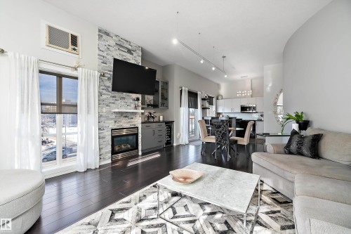 Living room with dark wood finished floors, a fireplace, rail lighting, and beverage cooler - 302 10905 109 Street, Edmonton, AB 