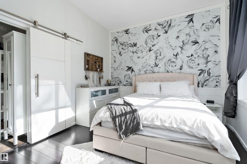 Bedroom featuring a barn door, wood finished floors, an accent wall, and wallpapered walls - 302 10905 109 Street, Edmonton, AB 