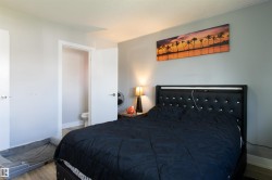 Bedroom featuring light gray walls, wood-finish flooring, a white ceiling, and a doorway revealing a partial view of a bathroom with a visible toilet - 