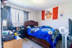 Bedroom featuring a window with dark curtains, a traditional wood-finish bed frame, and wood-finish flooring - 