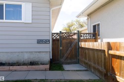 Private side entrance featuring a wooden gate with decorative metalwork, a full wooden privacy fence, and a concrete pathway - 
