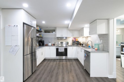U-shaped kitchen featuring white cabinetry, stainless steel appliances, grey subway tile backsplash, and wood-finish flooring - 7115 39A Avenue, Edmonton, AB - Indoor Photo Showing Kitchen With Upgraded Kitchen