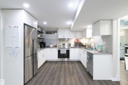 U-shaped kitchen featuring white cabinetry, stainless steel appliances, grey subway tile backsplash, and wood-finish flooring - 