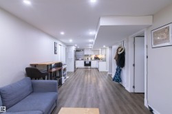 Open-concept living space featuring wood-finish flooring, recessed lighting, and a white kitchen with stainless steel appliances - 