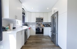 Modern kitchen featuring white cabinetry, stainless steel appliances, light-toned countertops, subway tile backsplash, and wood-finish flooring - 