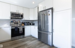 Kitchen featuring white shaker-style cabinetry, wood-finish flooring, stainless steel appliances, light-toned countertops, and a subway tile backsplash - 