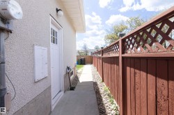 Side exterior with textured stucco finish, a white paneled door with window lites, and a concrete pathway - 