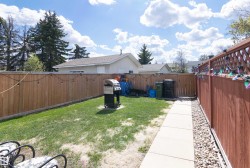 Fenced backyard featuring a manicured lawn, concrete pathway, and decorative gravel - 