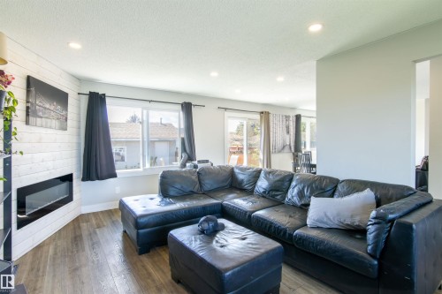 Living room featuring wood-finish flooring, recessed lighting, and a modern wall-mounted fireplace with shiplap surround - 7115 39A Avenue, Edmonton, AB - Indoor Photo Showing Living Room With Fireplace
