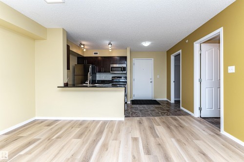 Open-concept living space featuring wood-finish flooring, a kitchen with dark cabinetry, black appliances, a raised breakfast bar, and recessed lighting - 404 12045 22 Avenue, Edmonton, AB 