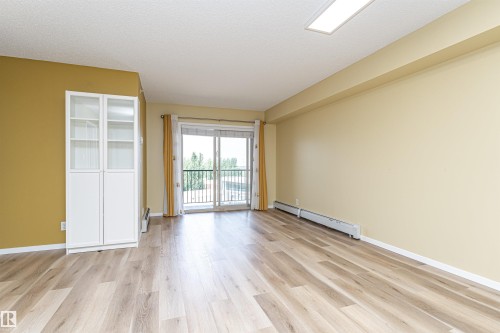Spacious room with wood-finish flooring, a full wall of warm yellow paint, and a white built-in display cabinet - 404 12045 22 Avenue, Edmonton, AB 