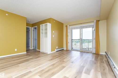 Spacious living area featuring wood-finish flooring, a built-in display cabinet, and a sliding glass door opening to a balcony with a metal railing - 404 12045 22 Avenue, Edmonton, AB 