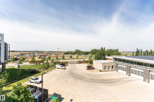 Paved parking area bordered by a structured building with multiple garage doors and a surrounding landscape featuring manicured lawns and trees - 404 12045 22 Avenue, Edmonton, AB 