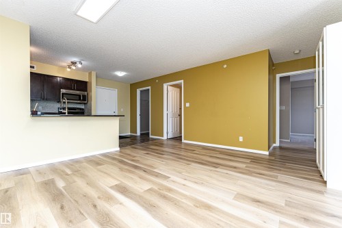 Open-concept living space featuring light wood-finish flooring, a kitchen counter bar, dark wood cabinetry, and stainless steel appliances - 404 12045 22 Avenue, Edmonton, AB 