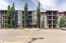 Contemporary multi-story building featuring stone-look facade accents, private balconies, abundant mature trees, a main entrance with prominent building numbering, and a dedicated parking area - 404 12045 22 Avenue, Edmonton, AB 